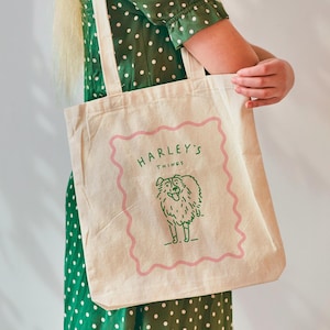 Op de afbeelding: Een witte canvas tote bag met een roze en groen ontwerp. Het ontwerp bevat een hond met de tekst "Harley's Things" erboven.