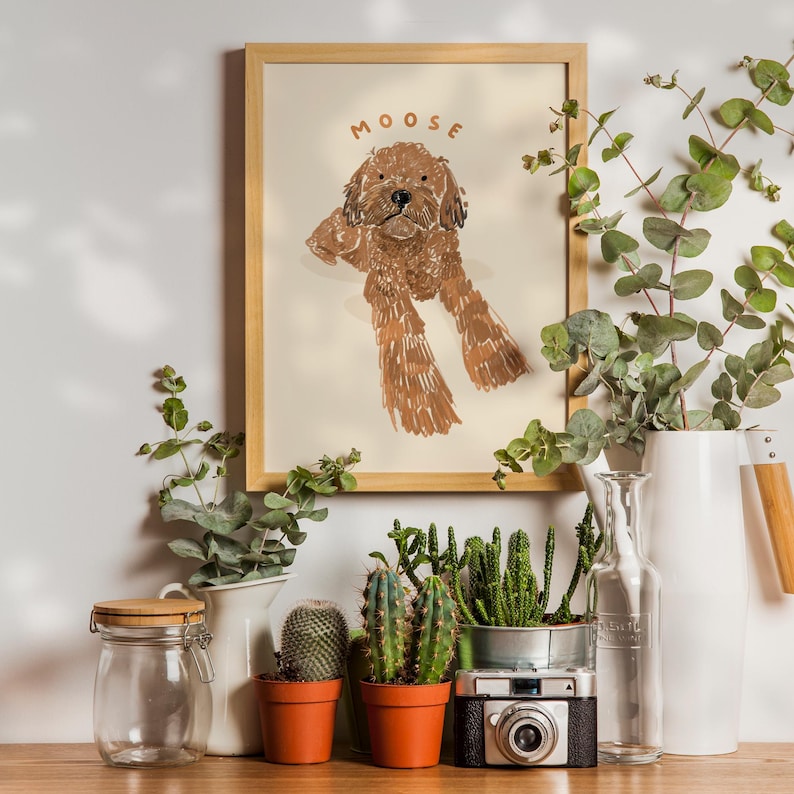 May include: A framed illustration of a brown dog with the name "MOOSE" written above it. The illustration is surrounded by plants and a white pitcher.