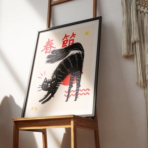 Puede incluir: Un gato negro con un sol rojo detr&aacute;s, estir&aacute;ndose con el texto "春節" en caracteres chinos rojos. El fondo es de color beige claro con una estrella amarilla.