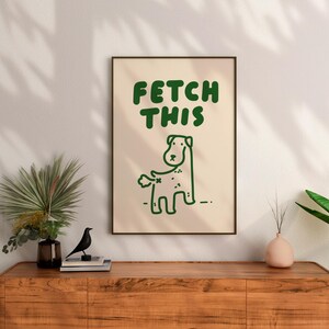 May include: A framed print with a green cartoon dog and the text "FETCH THIS" in green letters on a cream background.
