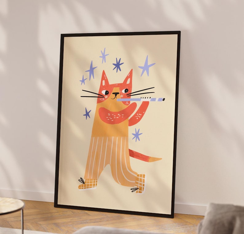 May include: A framed art print featuring a whimsical illustration of a cat playing a flute. The cat is orange and yellow, wearing striped pants, and surrounded by blue stars. The artwork has a playful, cartoonish style.