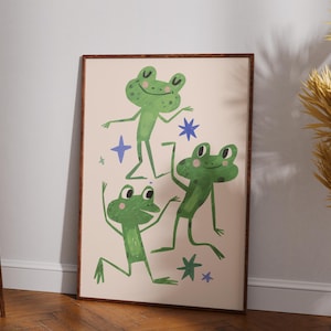 May include: A framed art print featuring three green cartoon frogs in various poses, with blue star accents on a cream background. The artwork has a whimsical, playful style, perfect for a child's room or a fun-loving space.