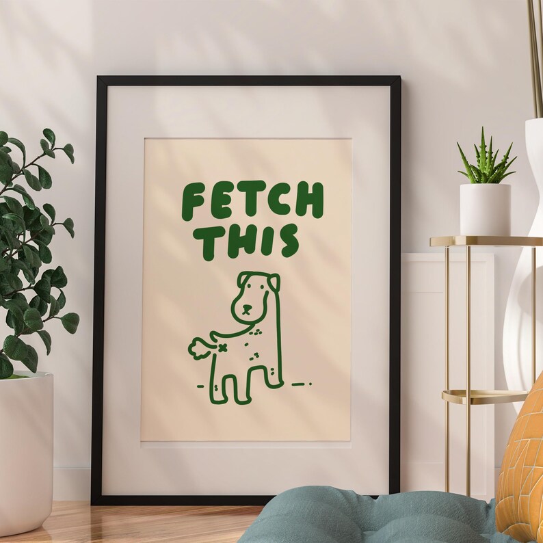 May include: A framed print with a cream background and green text that says "FETCH THIS". A cartoon green dog with a tail sticking out is below the text.