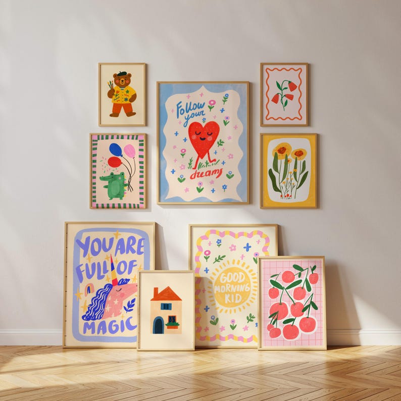 May include: A collection of framed art prints with colorful illustrations. The prints feature a bear, a crocodile with balloons, a heart with legs, flowers, a unicorn, a house, cherries, and the text "YOU ARE FULL OF MAGIC" and "GOOD MORNING KID".