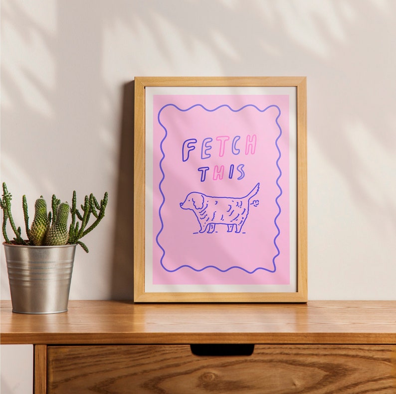 May include: A framed print with a pink background and a white border. The print features a cartoon dog with the text "FETCH THIS" in purple and pink letters.