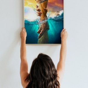 May include: A framed painting depicting a hand reaching out from the water to grasp another hand. The painting is set against a backdrop of a sunset sky and a stormy sea.