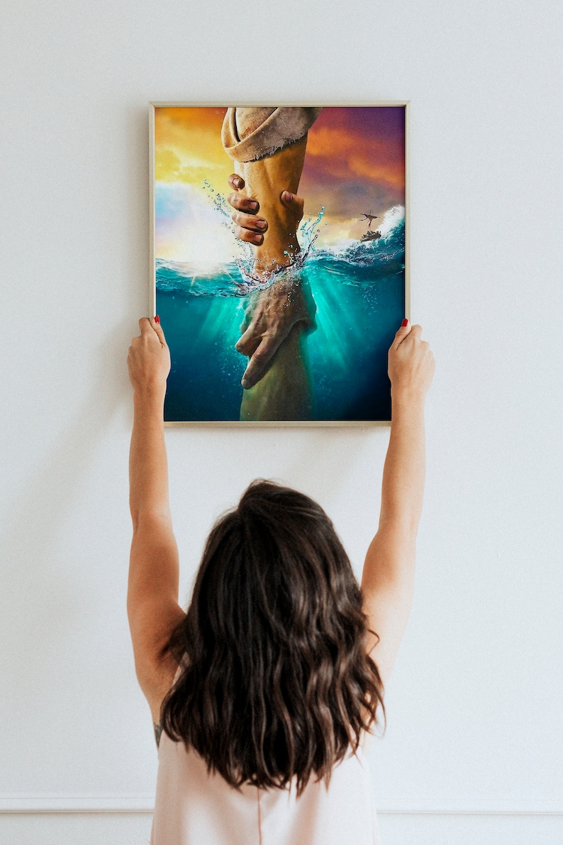 May include: A framed painting depicting a hand reaching out from the water to grasp another hand. The painting is set against a backdrop of a sunset sky and a stormy sea.