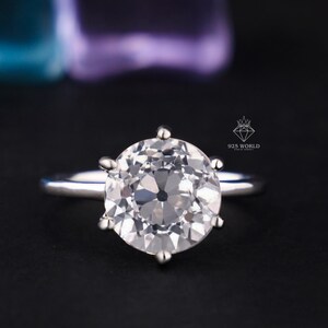 May include: A silver-toned ring featuring a large, round, brilliant-cut clear stone held by six prongs on a smooth, polished band. The small logo text 925 WORLD is visible near the setting, indicating the metal composition of this jewelry piece.