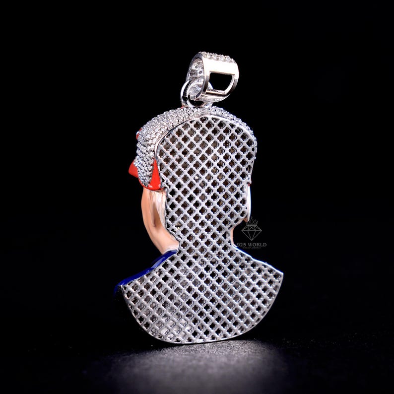 May include: A silver pendant with a detailed design of a person's profile. The pendant features a red and blue accent, with a lattice-like pattern on the back. The top of the pendant is encrusted with small, sparkling stones.