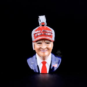 May include: A pendant featuring a detailed bust of a man wearing a red baseball cap with the text "Make America Great Again". The pendant has a red, white, blue, and silver color scheme and is set against a black background.