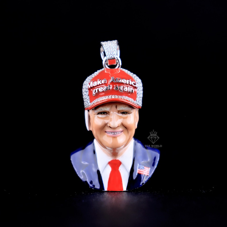 May include: A pendant featuring a detailed bust of a man wearing a red baseball cap with the text "Make America Great Again". The pendant has a red, white, blue, and silver color scheme and is set against a black background.