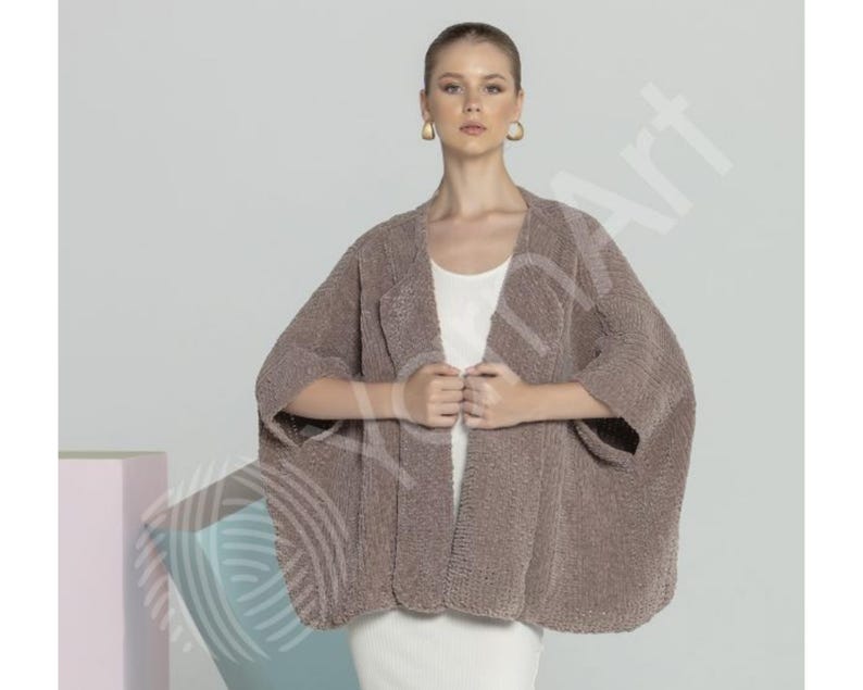 May include: A brown, open-front cardigan with wide sleeves. The soft, textured knitwear is worn over a white top and a white skirt. The cardigan is a neutral colour, suitable for layering.