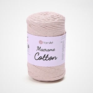 May include: A light beige spool of YarnArt Macrame Cotton yarn. The label features the brand name and product information. The tightly wound yarn suggests it's suitable for various crafting projects, such as macrame.