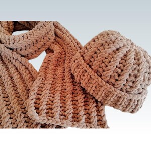 Pode incluir: Um conjunto de cachecol e gorro de malha numa cor bege neutra e quente. O cachecol &eacute; longo e largo, com uma malha espessa e texturizada. O gorro &eacute; de estilo justo, tamb&eacute;m com uma malha texturizada. O conjunto &eacute; feito de um fio macio e grosso.