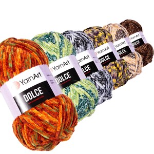 May include: A selection of YarnArt Dolce yarn skeins in a range of colours. The yarn has a soft, velvety texture and comes in shades of orange, green, grey, yellow, and brown. Each skein is labelled with the word "DOLCE".
