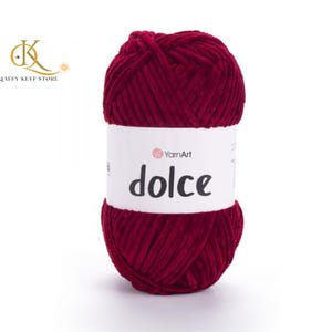 May include: A ball of deep red yarn with a white label that reads "dolce" in black text. The yarn is thick and appears soft. The brand name "YarnArt" is also visible on the label. This yarn is suitable for knitting and crochet projects.