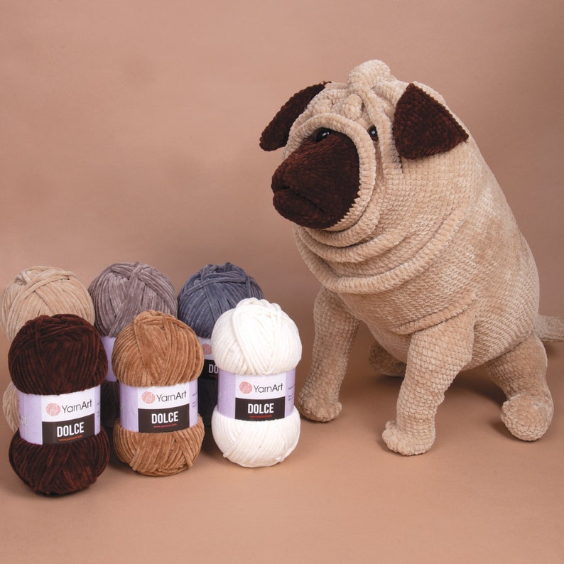 May include: A soft toy Shar Pei dog in beige, alongside several balls of YarnArt Dolce yarn in shades of brown, grey, and white. The yarn is velvety, ideal for crafting. The dog features brown detailing.