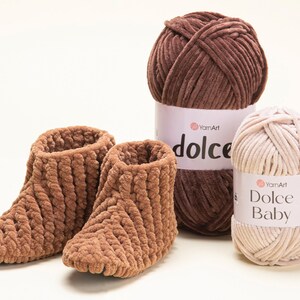 May include: Two brown, plush, knitted slippers are next to two balls of yarn. One ball is a dark brown colour, and the other is a light beige colour. The yarn labels read "YamArt dolce" and "YamArt Dolce Baby".