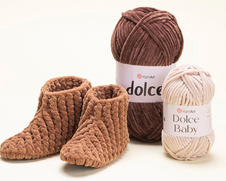 May include: Two brown, plush, knitted slippers are next to two balls of yarn. One ball is a dark brown colour, and the other is a light beige colour. The yarn labels read "YamArt dolce" and "YamArt Dolce Baby".