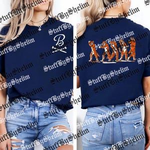 May include: Navy blue t-shirt with a white "B" and crossed baseball bats on the front. The back features a graphic of orange and black tigers. The shirt is a casual wear item.