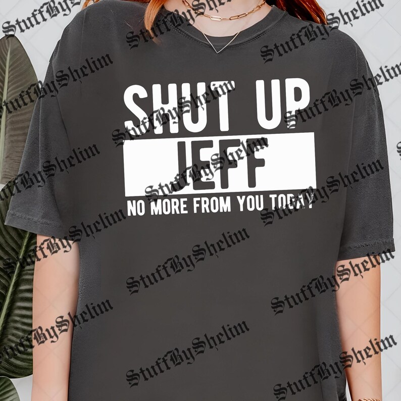 May include: Dark gray t-shirt with the text "SHUT UP JEFF" in large white letters. Below the name is the phrase "NO MORE FROM YOU TODAY". The shirt is a casual style.