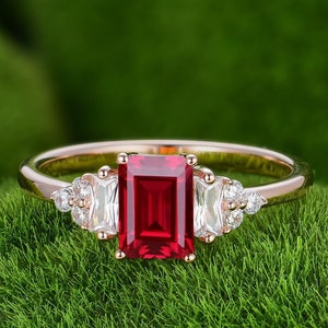 May include: A rose gold ring with a large, emerald-cut ruby gemstone surrounded by smaller, white diamonds.