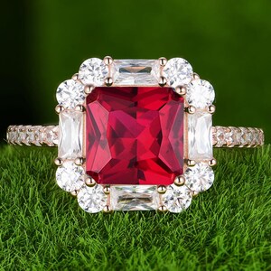 May include: A square-shaped ruby ring with a halo of smaller diamonds. The ring is set in rose gold and has a pave setting.
