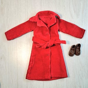 May include: A red corduroy coat with a matching belt and a pair of brown shoes. The coat has a collar and buttons down the front. The shoes are small and have a rounded toe.