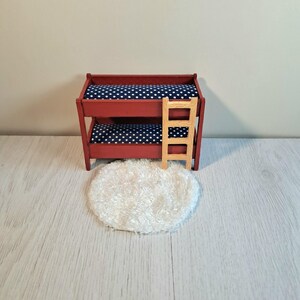 May include: Miniature red bunk bed with navy blue and white polka dot bedding. A small wooden ladder is attached to the side. A fluffy white rug sits in front of the bed. This dollhouse furniture is perfect for a child's room.