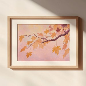 Puede incluir: Una impresión enmarcada de una pintura de acuarela que representa una rama de hojas de otoño en tonos naranja y amarillo sobre un fondo rosa y morado.