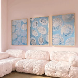 May include: Three framed prints of blue and white seashells hang on a pale pink wall above a white modular sectional sofa.