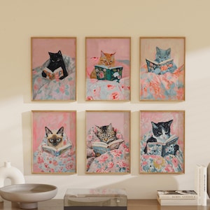 Op de afbeelding: Zes ingelijste prints van katten die in bed boeken lezen. Elke print toont een ander kattenras en een andere boekomslag. De prints zijn allemaal in een vergelijkbare stijl, met een roze achtergrond en een bloemenpatroon.