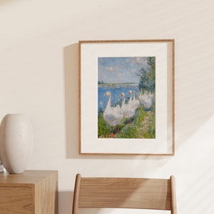 May include: A framed painting of a group of white geese walking along a grassy path by a body of water. The geese are in a line, with the one at the front looking directly at the viewer. The painting is done in a realistic style, with a focus on the details of the geese's feathers and the surrounding landscape.