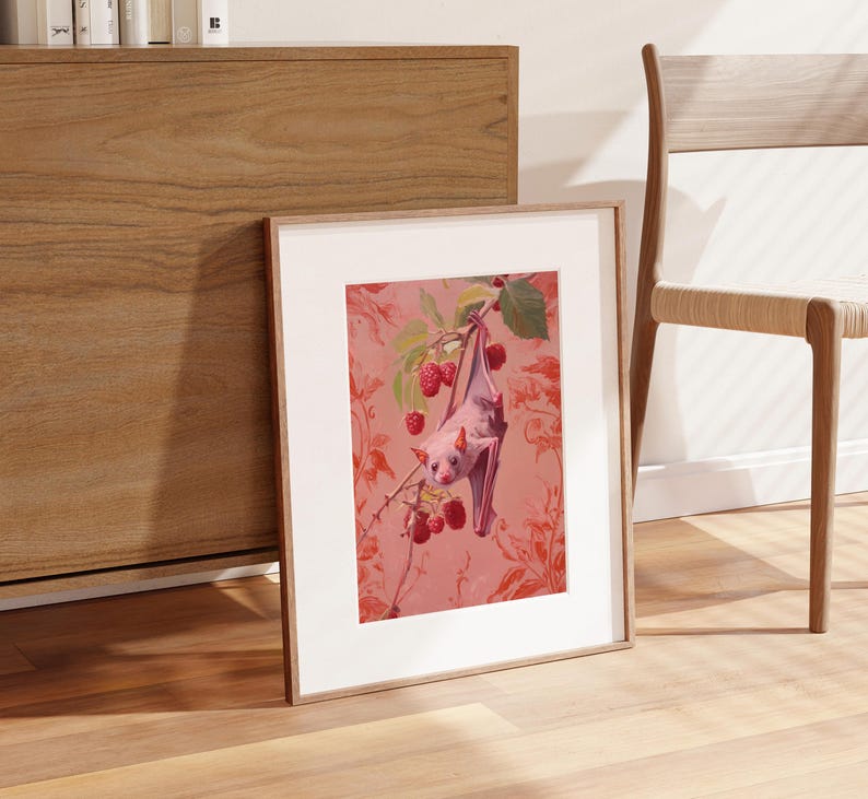 May include: A framed print of a pink bat hanging upside down from a branch of a pink flowering tree. The background is a pink floral pattern.