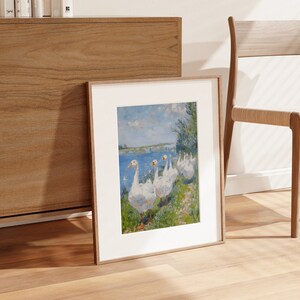 May include: A framed print of a painting depicting a group of white geese walking in a line on a grassy bank by a body of water. The geese are facing the right side of the image. The background is a blue sky with white clouds and a green field.