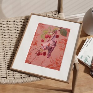 May include: A framed print of a pink bat hanging upside down from a branch with red berries. The bat is in a pink and white floral pattern.
