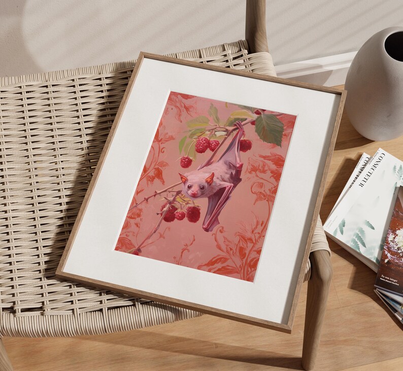May include: A framed print of a pink bat hanging upside down from a branch with red berries. The bat is in a pink and white floral pattern.