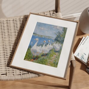 May include: A framed print of a painting depicting a group of white geese walking along a riverbank. The geese are in a line, with their heads down, and their feathers are ruffled. The background is a blue sky with white clouds, and the river is a light blue color. The painting is in a simple wooden frame.