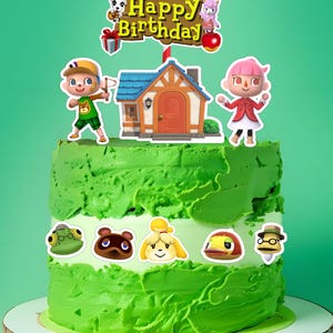 Peut inclure: Un gâteau à deux étages vert et blanc décoré de personnages d'Animal Crossing. L'étage supérieur présente une maison, un personnage de garçon et une fille, et une bannière qui dit "Joyeux anniversaire". L'étage inférieur présente quatre personnages : une grenouille, un raton laveur, un chien et un canard.