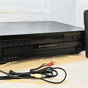 Puede incluir: Reproductor de CD Sony negro con mando a distancia y cables de audio. El reproductor de CD tiene una función de cambiador de CD y una toma de auriculares. El mando a distancia es negro con varios botones. Los cables de audio tienen conectores rojo y blanco.