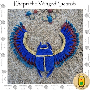 Puede incluir: Un escarabajo alado Khepri tejido a ganchillo con cuerpo azul, bordes dorados y alas extendidas en hilo azul, dorado y granate. La pieza se muestra junto a un pequeño colgante de escarabajo de metal con colores a juego.
