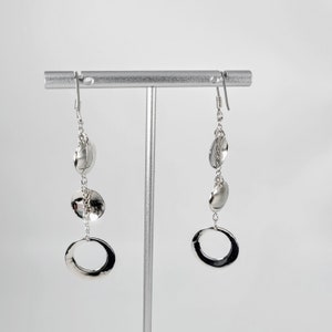 Peut inclure: Boucles d'oreilles pendantes en argent avec trois disques ronds et un grand anneau ovale en bas.