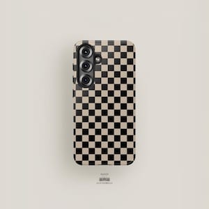 May include: A phone case featuring a black and beige chequered design. The case has a triple-lens camera module. The brand name "MAISON ACCESSOBELLE" is printed at the bottom.