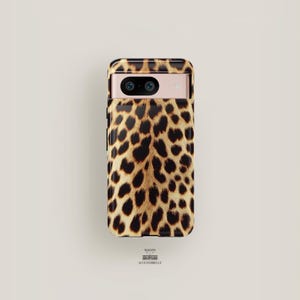 Può includere: Una custodia per telefono nera con un design a stampa leopardata. La custodia ha un rialzo per la fotocamera e un ritaglio per la porta di ricarica del telefono.