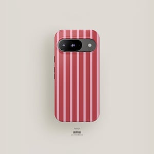 May include: A phone case with a vertical stripe pattern in red and pink. The case has a camera cutout and buttons on the side. The stripes alternate between a darker red and a lighter pink. The text "MAISON ACCESSOBELLE" is at the bottom.