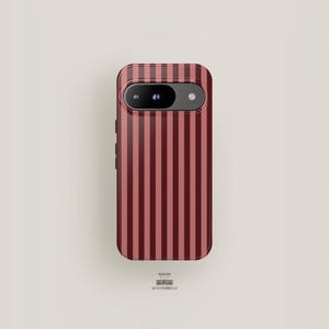 Może przedstawiać: Burgundowa i jasno czerwona obudowa telefonu w paski. Obudowa ma wycięcie na aparat i boczne przyciski. Tekst "MAISON ACCESSOBELLE" znajduje się na dole.