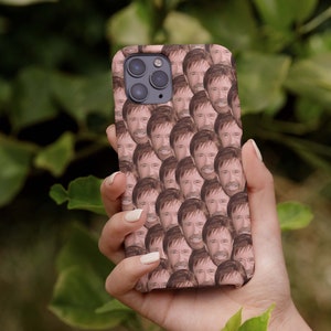 May include: A phone case with a repeating pattern of a man's face. The case is pink and the man has brown hair and a beard.