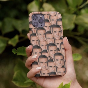 Puede incluir: Una funda de teléfono con una imagen repetida de la cara de un hombre. La funda es marrón y la cara del hombre es de piel clara.