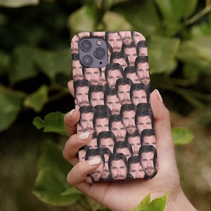 May include: A pink phone case with a repeated pattern of a man's face. The case is being held in a hand.