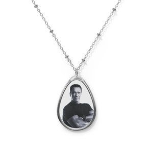 May include: A silver chain necklace with a teardrop-shaped pendant featuring a black and white photo of a man.